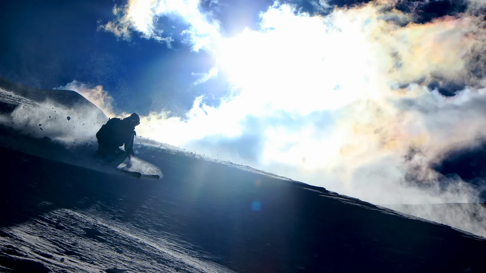 Um esquiador em contraluz ao sol, levantando uma nuvem de neve fresca